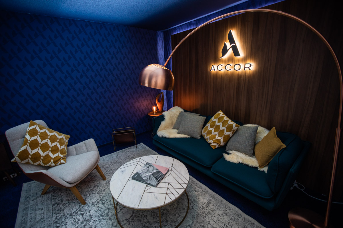 Accor at IHIF Berlin 2021 — Branding Illuminated Accor logo above a sofa and round table in the blue lounge at IHIF Berlin 2021