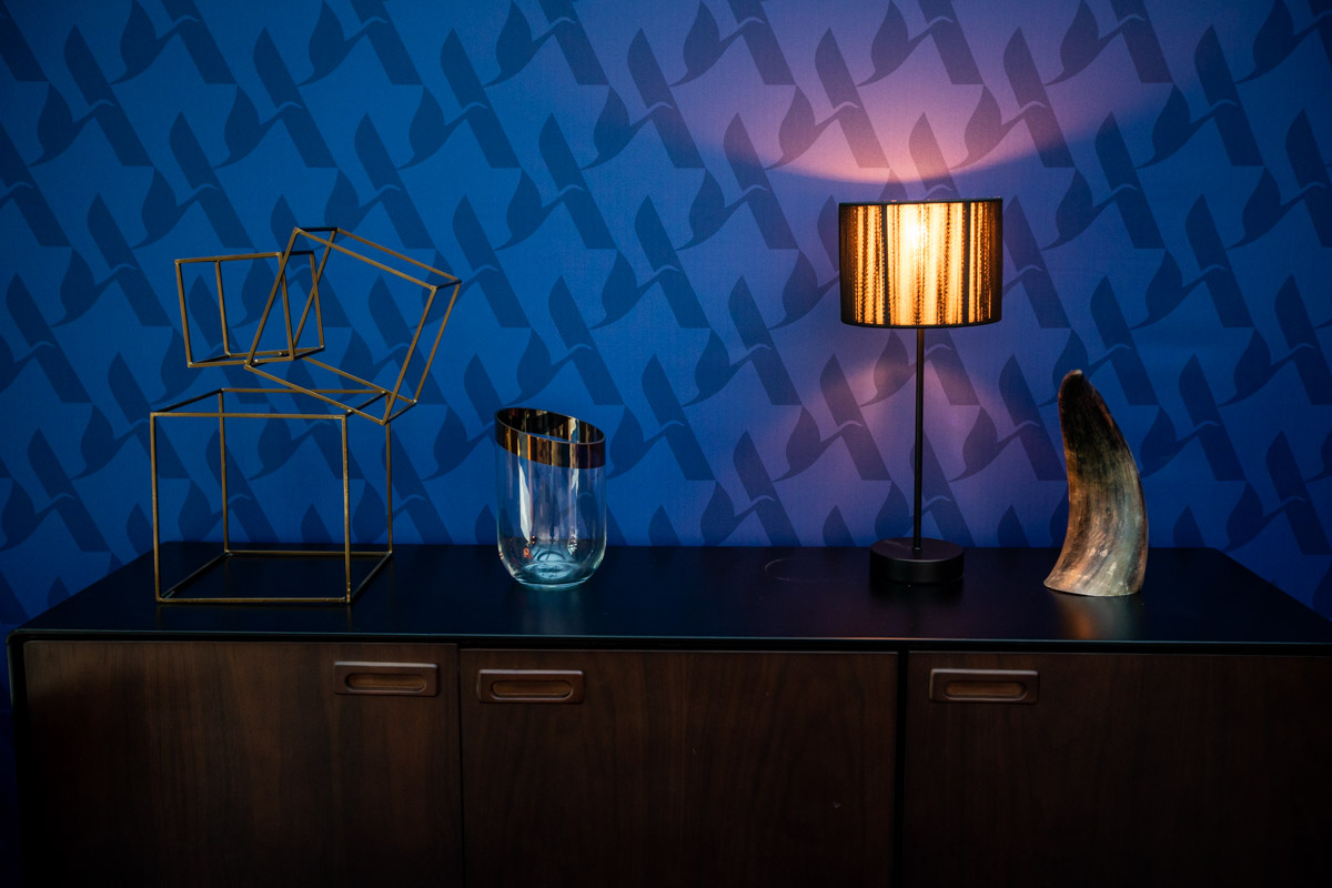 Accor at IHIF Berlin 2021 — Interior detail Table lamp, glassware and decorative objects against a blue patterned wall at IHIF Berlin 2021